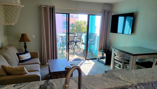 A living room with a sofa, a coffee table, a TV, and a balcony with outdoor furniture.