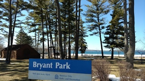 A sign for Bryant Park with a view of tall trees and a body of water in the background. - Modern Mid-Town  Condo (Downtown Traverse City) (Traverse City)