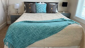 A neatly made bed with a teal blanket, a patterned headboard, and two bedside tables with lamps. - Modern Mid-Town  Condo (Downtown Traverse City) (Traverse City)