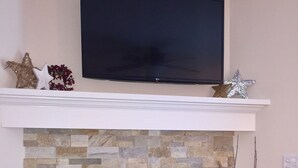 A fireplace with a stone facade, a mounted television above it, and decorative items on the mantel. - Modern Mid-Town  Condo (Downtown Traverse City) (Traverse City)