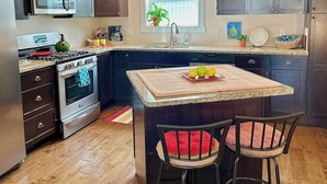 A modern kitchen with dark cabinets, stainless steel appliances, a central island with a marble countertop, and a window with a view of greenery. - Modern Mid-Town  Condo (Downtown Traverse City) (Traverse City)