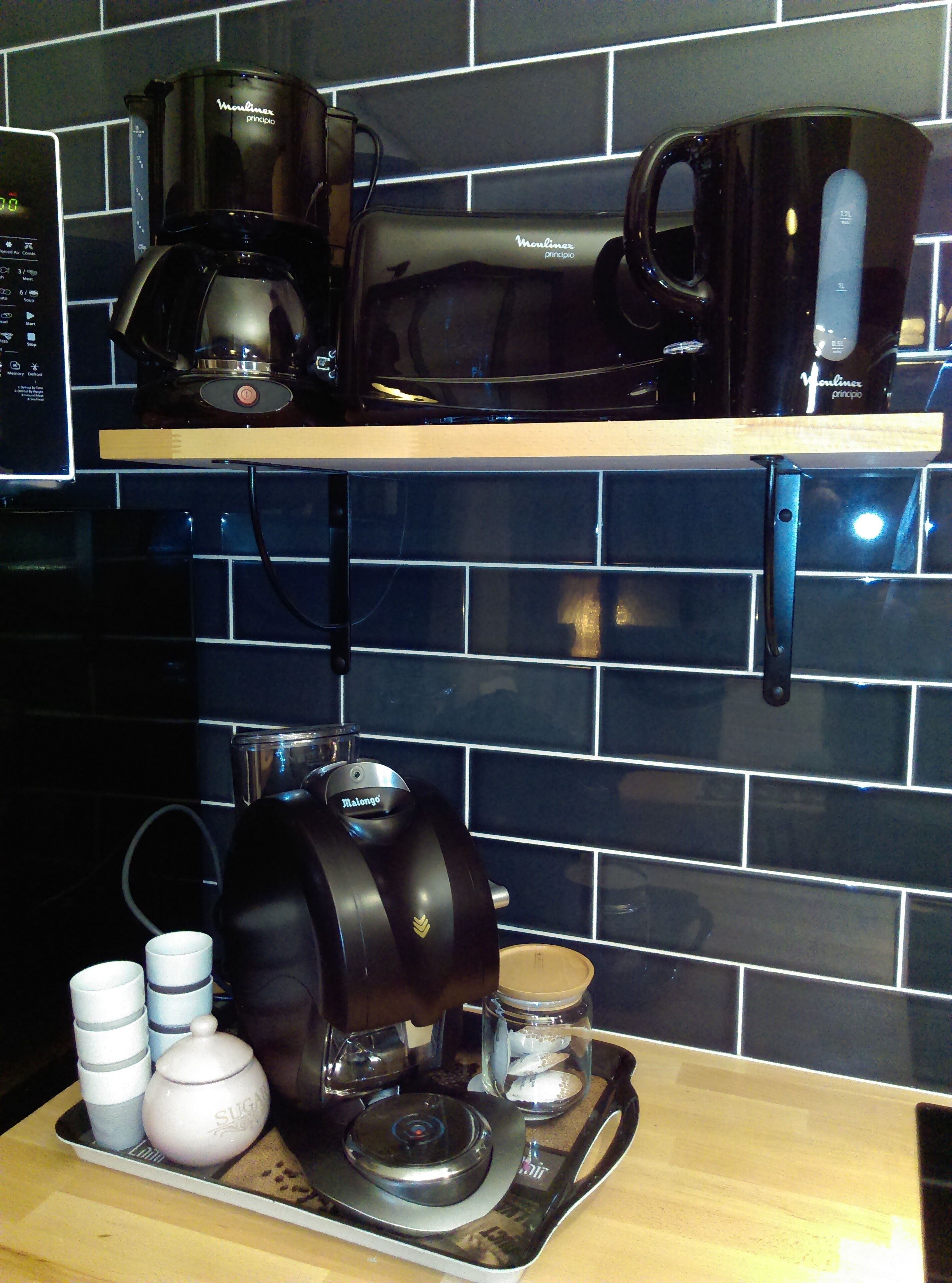 Een keuken met een koffiezetapparaat, waterkoker en een dienblad met bekers en een suikerpot.