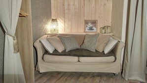 A cozy living room with a beige sofa, patterned cushions, a wooden wall panel, a wall-mounted lamp, and a framed picture. - very nice studio with real quiet bed at 1400m. from the center and the beaches (Menton)