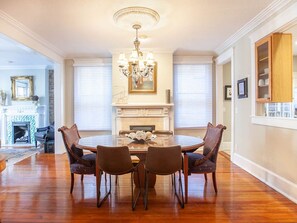 A dining room with a round table, four chairs, a chandelier, and a fireplace.