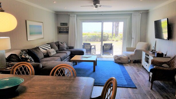A living room with a sofa, coffee table, and chairs, a dining table with chairs, and a view through a glass door to the outdoors.