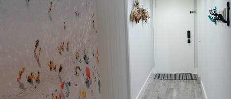 A hallway with a large abstract painting on the left wall, a door at the end, and a modern light fixture above it.