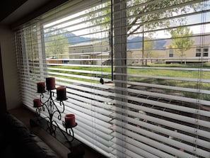 A room with a large window with horizontal blinds, a black leather sofa, and a candle holder with candles. - 3 Lazy H Yellowstone Lodging - Just Blocks from Yellowstones North Entrance (Gardiner)