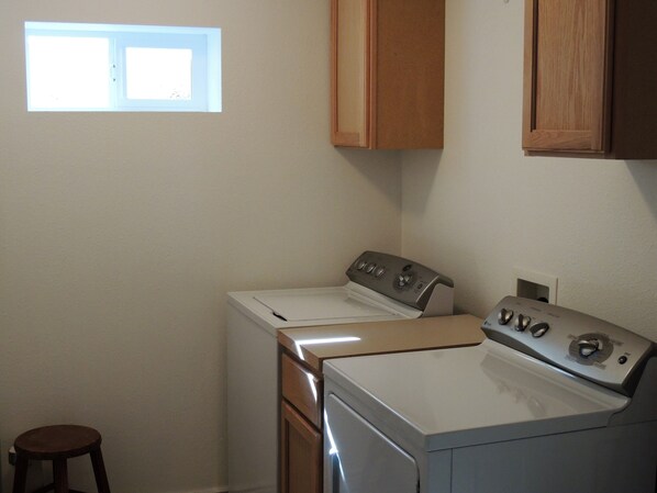 A laundry room with a washing machine, dryer, and a small stool. - 3 Lazy H Yellowstone Lodging - Just Blocks from Yellowstones North Entrance (Gardiner)