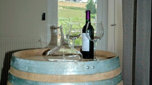 Un tonneau en bois sur lequel sont posés une bouteille de vin et deux verres à vin, le tout placé près d’une fenêtre donnant sur un vignoble.