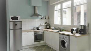 Une cuisine compacte équipée d’un four à micro-ondes, d’un four traditionnel, d’un lave-linge et d’une fenêtre laissant entrer la lumière naturelle.