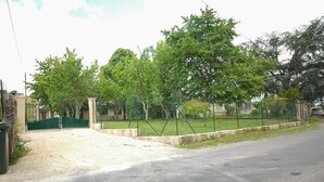 Un lotissement résidentiel fermé, avec une allée de gravier menant à un portail vert, entouré d’arbres et d’une clôture.