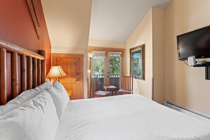 A hotel room with a bed, a TV, a lamp, a wooden door, and a view of the outdoors.