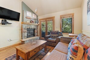A living room with a stone fireplace, a flat-screen TV, a sofa, and a window with a view of greenery.