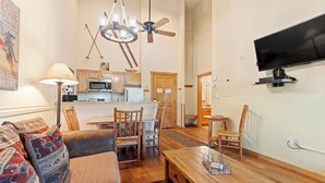 Un salon comprenant un canapé, une table à manger, des chaises, un lustre, un ventilateur de plafond, un téléviseur et un coin cuisine.