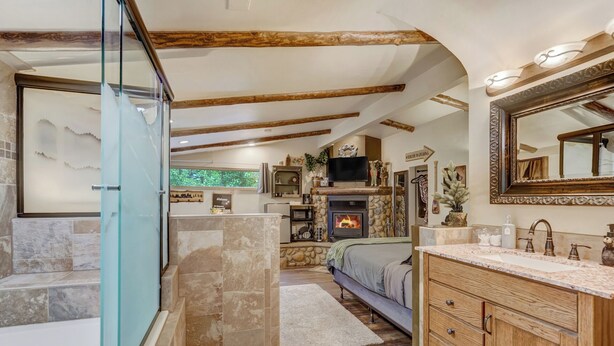 Un baño con cabina de ducha de vidrio, zona de ducha con suelo de piedra, tocador de madera con espejo y chimenea.