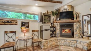 Una sala de estar acogedora con chimenea de piedra, un televisor de pantalla plana y un comedor con una mesa redonda y sillas.