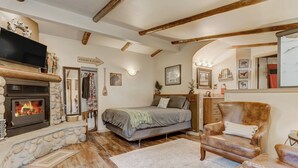Un cuarto acogedor con chimenea de piedra, una cama, un sillón de cuero y techo de madera.