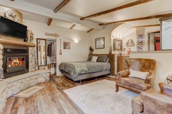 Um quarto acolhedor com lareira de pedra, uma cama, uma poltrona de couro e teto de madeira.