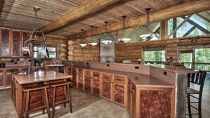 Een ruime keuken met een groot eiland, houten kastjes en een hoge plafond met zichtbare balken.