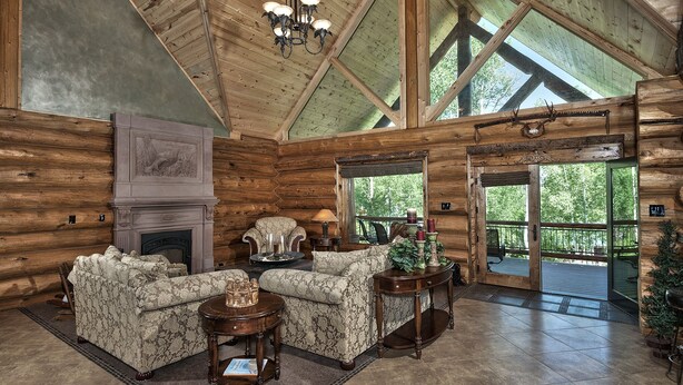 Een houten blokhut van binnen met een open haard, twee gestreepte banken, een kroonluchter en een groot raam.
