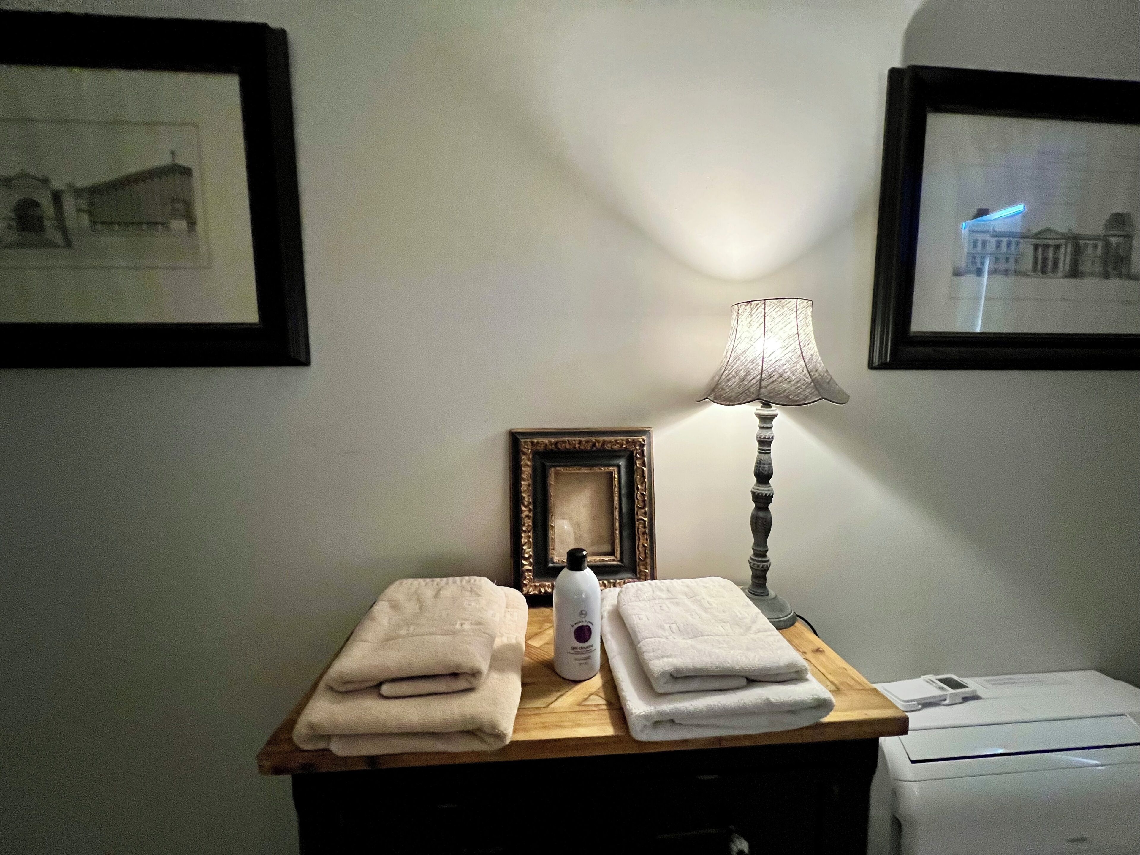 A room with a wooden table holding folded towels, a lamp, and a framed picture.