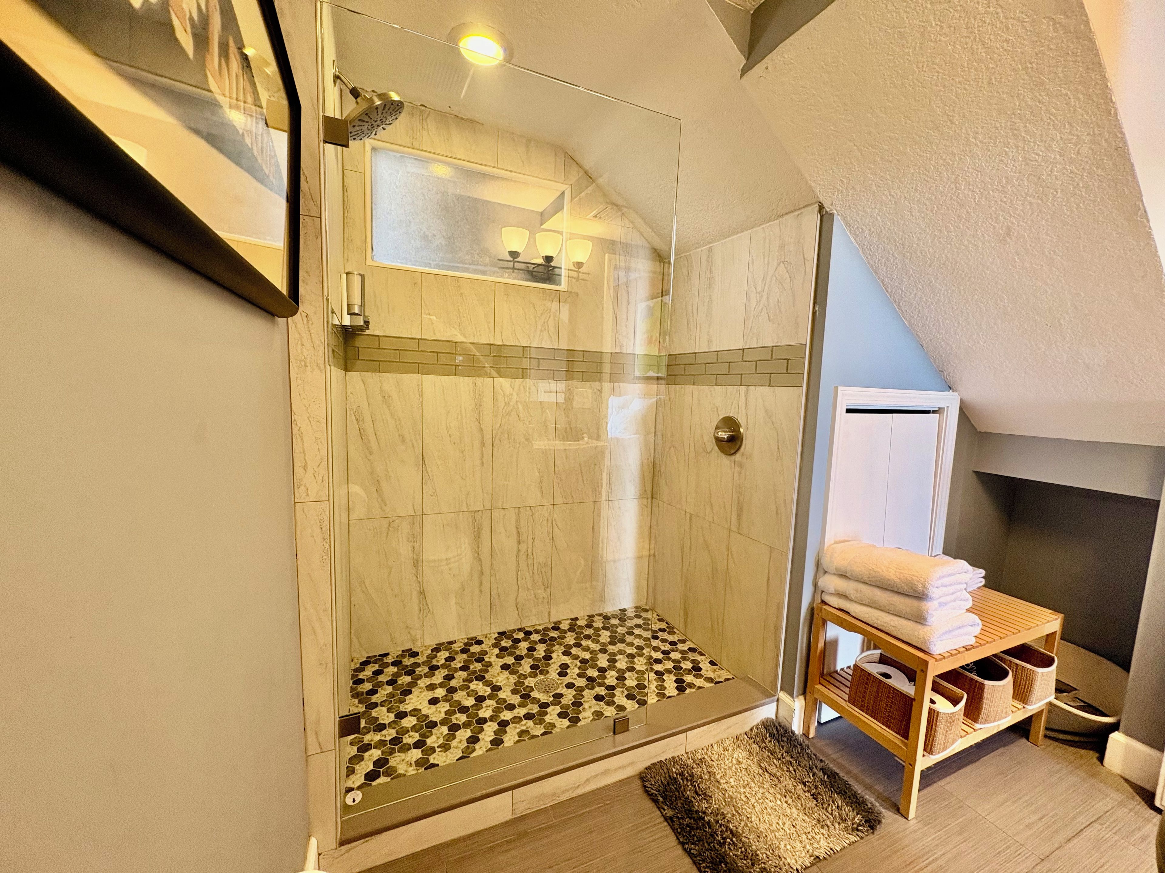 Ein modernes Badezimmer mit einer gläsernen Duschkabine, Fliesenboden und einem Holzbodenregal mit Handtüchern.