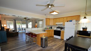 A spacious kitchen with wooden cabinets, a large island with stools, a ceiling fan, and a dining area with a table and chairs. - Waterfront Tranquil Escape-Single Family/Gated Community/Pool/Tennis Courts  (Lewes)