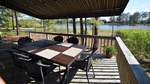 A covered outdoor deck with a table and chairs, overlooking a lake. - Waterfront Tranquil Escape-Single Family/Gated Community/Pool/Tennis Courts  (Lewes)