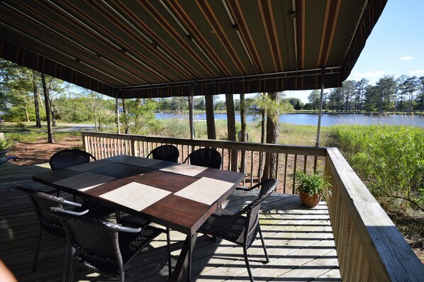 A covered outdoor deck with a table and chairs, overlooking a lake.
