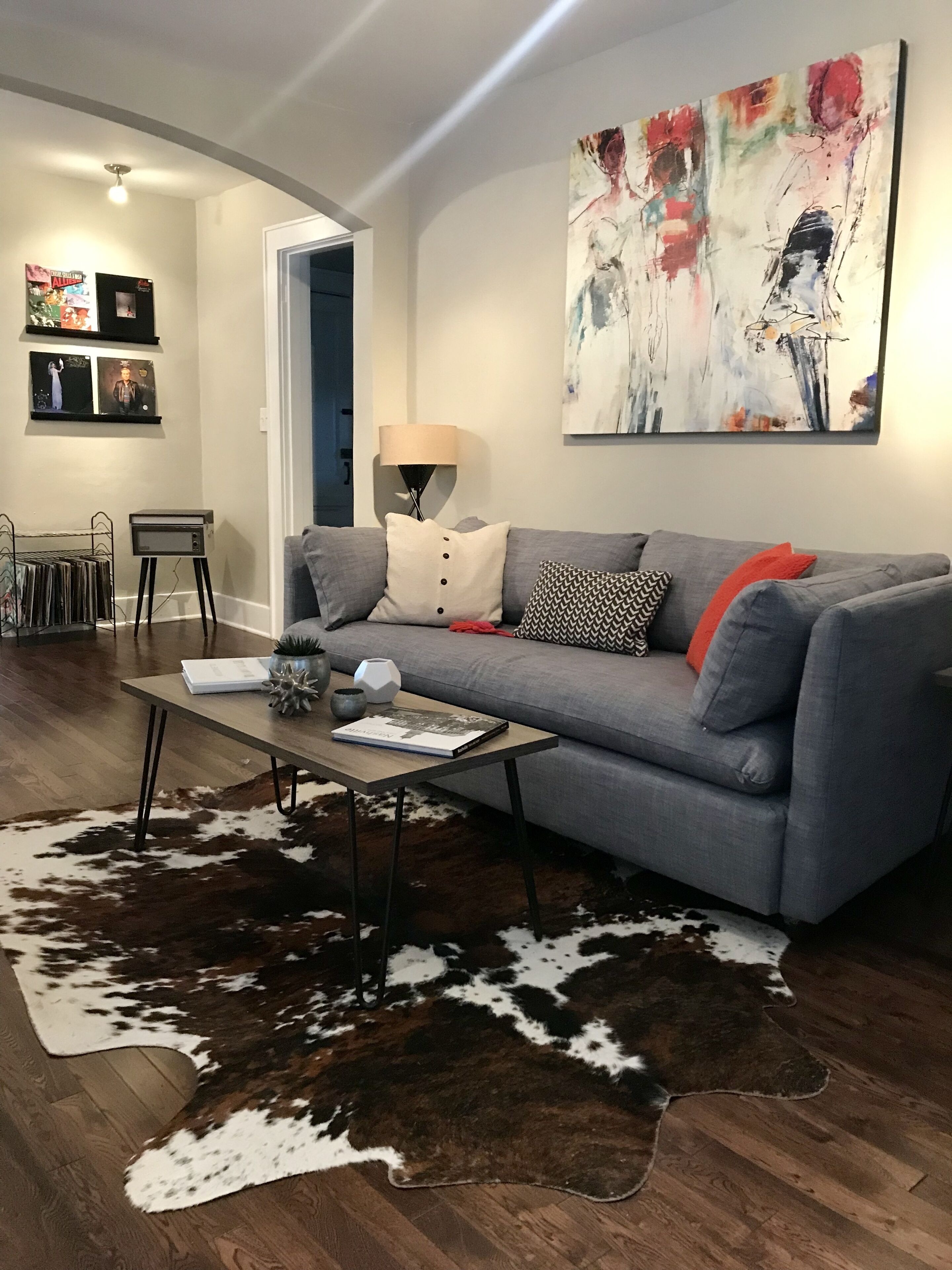 A modern living room with a grey sofa, a coffee table, and a large abstract painting on the wall.