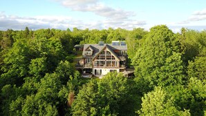 A large, two-story house surrounded by dense forest, with a prominent front deck and large windows. - BIG Family & Multi-Family Cottage with Incredible View, Hot Tub & Sauna (Dunchurch)