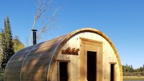 A wooden barrel-shaped cabin with a door and windows, situated on a wooden deck by a body of water. - BIG Family & Multi-Family Cottage with Incredible View, Hot Tub & Sauna (Dunchurch)
