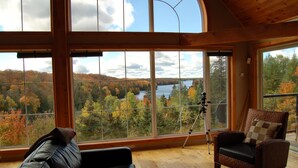 A room with large windows offering a view of a lake and autumn foliage. - BIG Family & Multi-Family Cottage with Incredible View, Hot Tub & Sauna (Dunchurch)