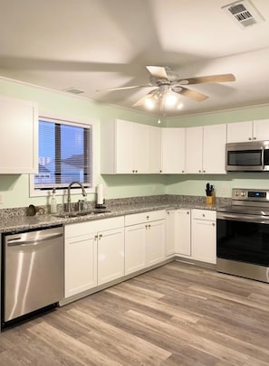 A kitchen with white cabinets, a granite countertop, stainless steel appliances, and a ceiling fan.