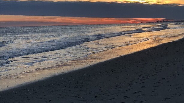 A beach with footprints leading to the water, a clear sky, and a sunset.