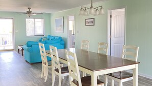 A spacious dining area with a wooden table and chairs, a blue sofa, and a ceiling fan.