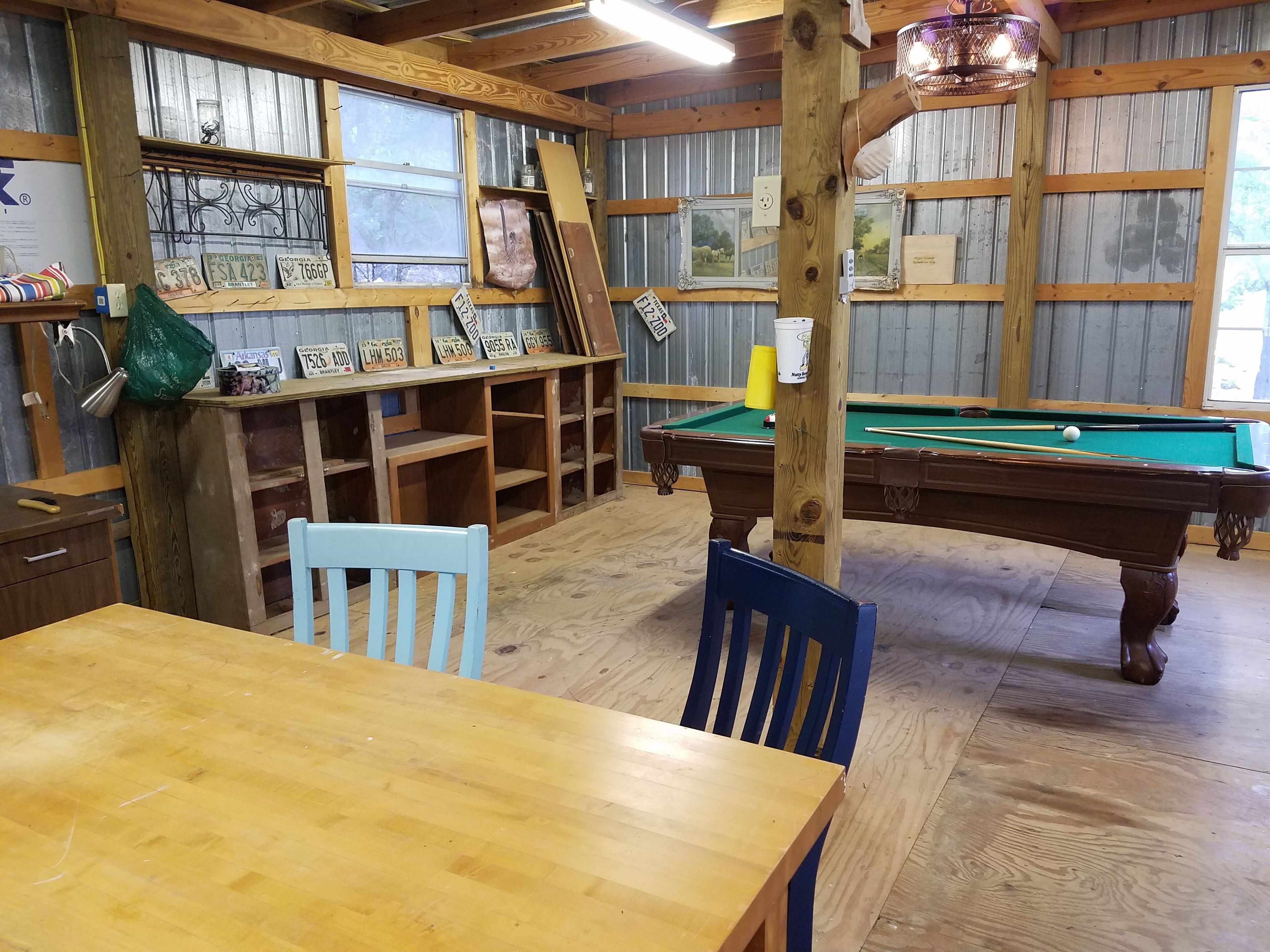 Une table de billard dans une pièce aux murs en bois, avec une table en bois et des chaises.