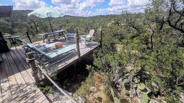 A deck with outdoor seating, a table, and a chair. - Secluded Waterfront Cabin- Canoe, Fish, Swim & Stargaze near Pedernales Falls (Dripping Springs)