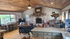 A spacious kitchen with a stone fireplace, wooden ceiling, and a large island counter. - Secluded Waterfront Cabin- Canoe, Fish, Swim & Stargaze near Pedernales Falls (Dripping Springs)