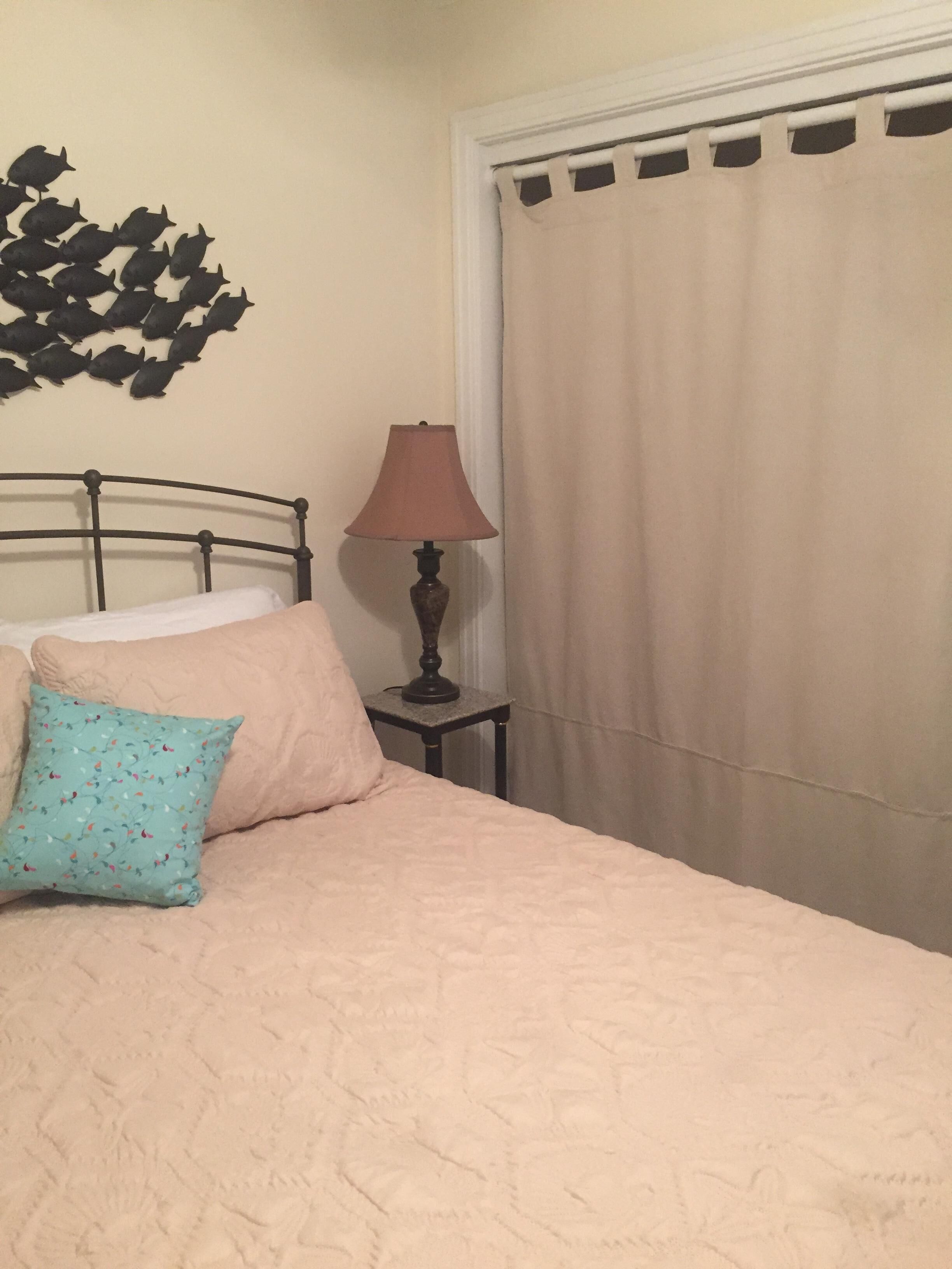 Un lit avec une couette beige, un oreiller turquoise et une petite table de chevet avec une lampe.