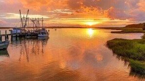 Ein ruhiger Fluss mit vertäuten Booten links, ein kleines Boot im Vordergrund und ein Sonnenuntergang im Hintergrund.