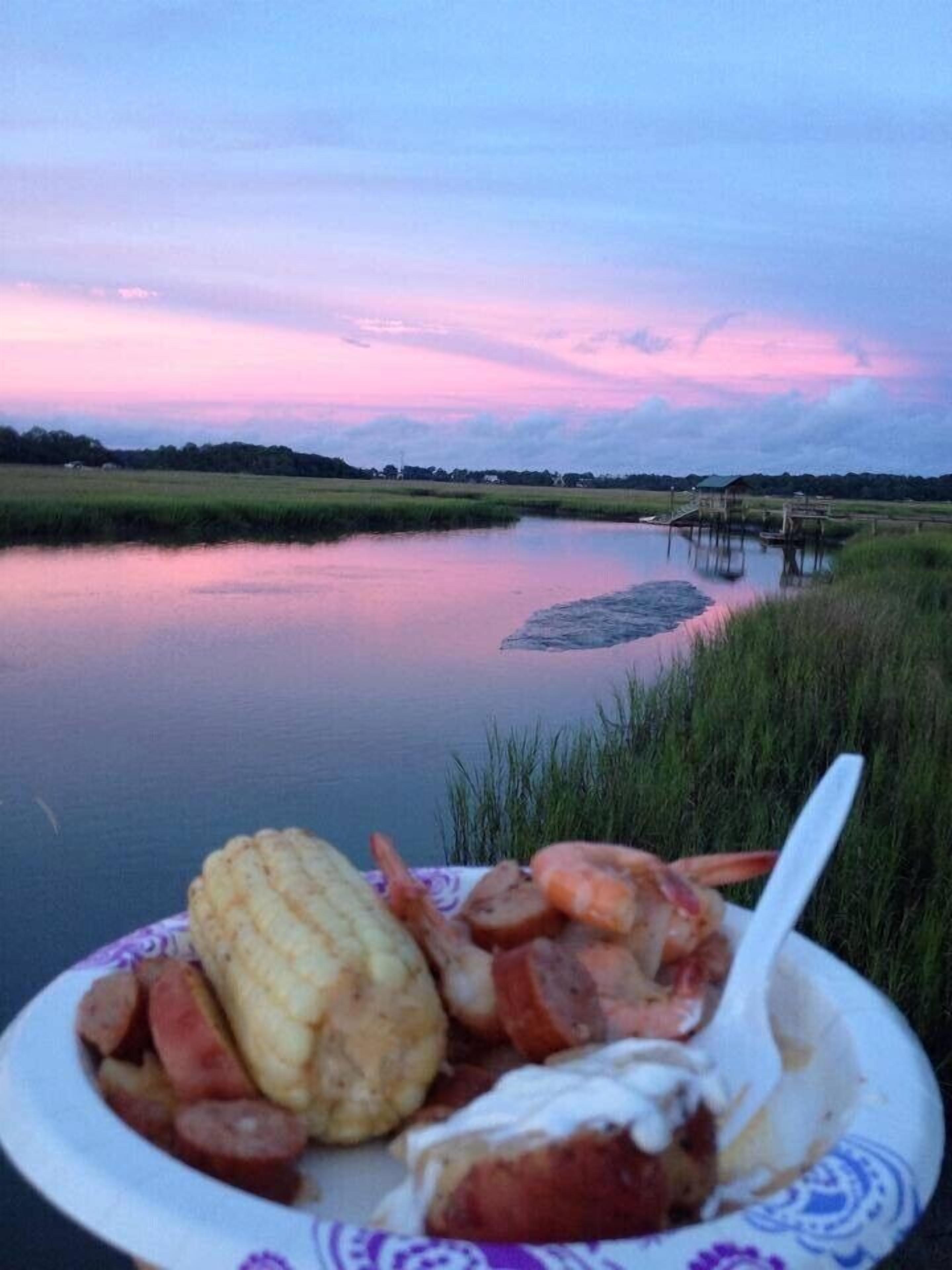 Una vista tranquila de un lago al atardecer, un muelle de madera y un plato de comida en primer plano.