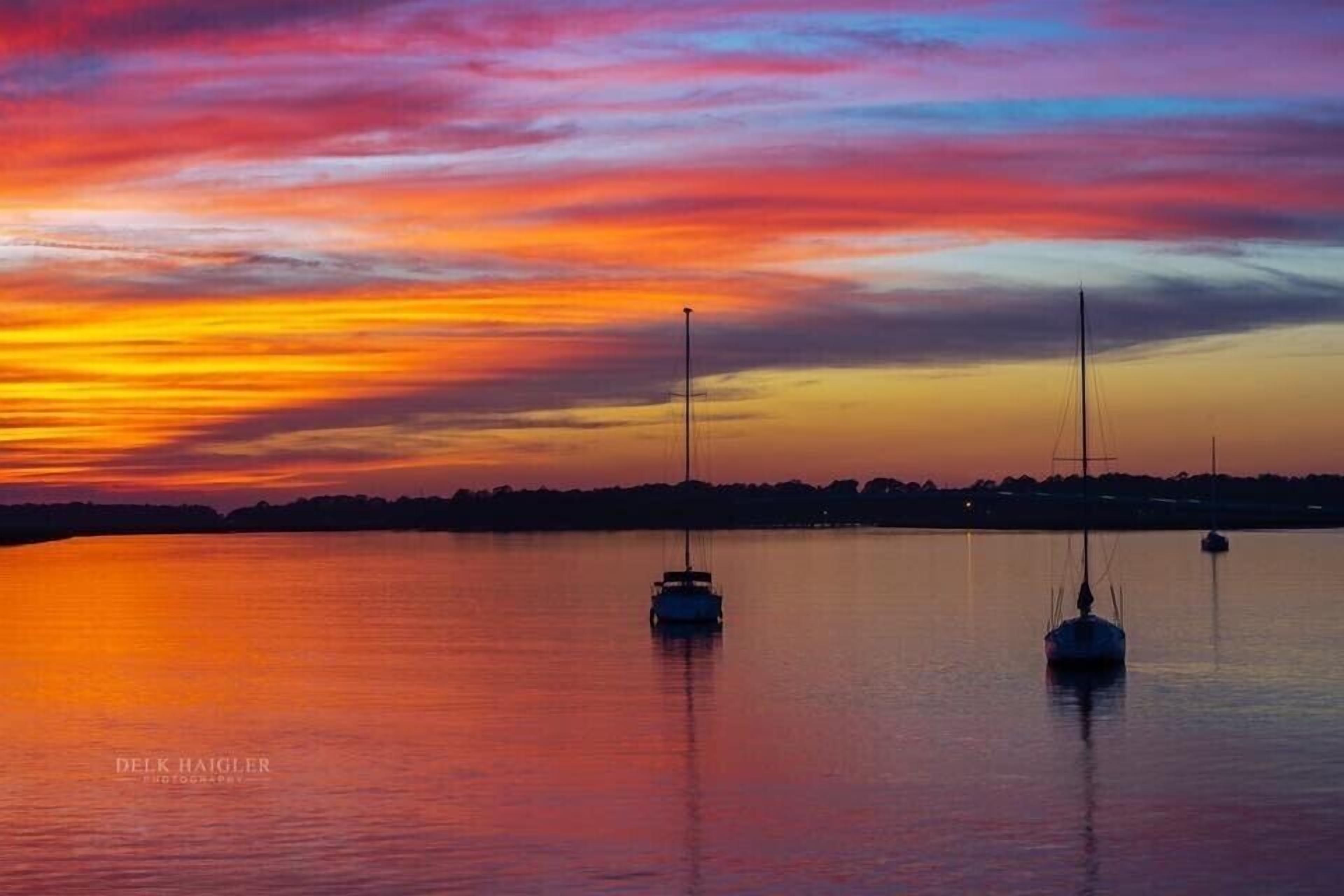 Atardecer sobre un cuerpo de agua en calma con dos veleros anclados.