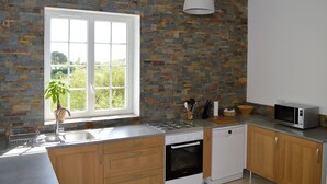 Eine moderne Küche mit Steinrückwand, Holzschränken, integriertem Backofen, Mikrowelle und einem Fenster mit Blick ins Grüne.