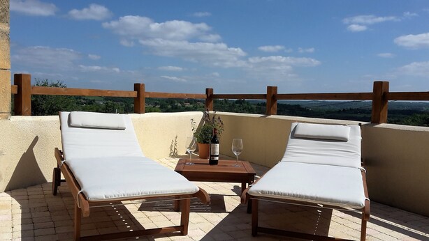Eine Terrasse mit zwei Liegestühlen, einem kleinen Tisch, einer Weinflasche und zwei Gläsern, sowie einem Blumentopf.