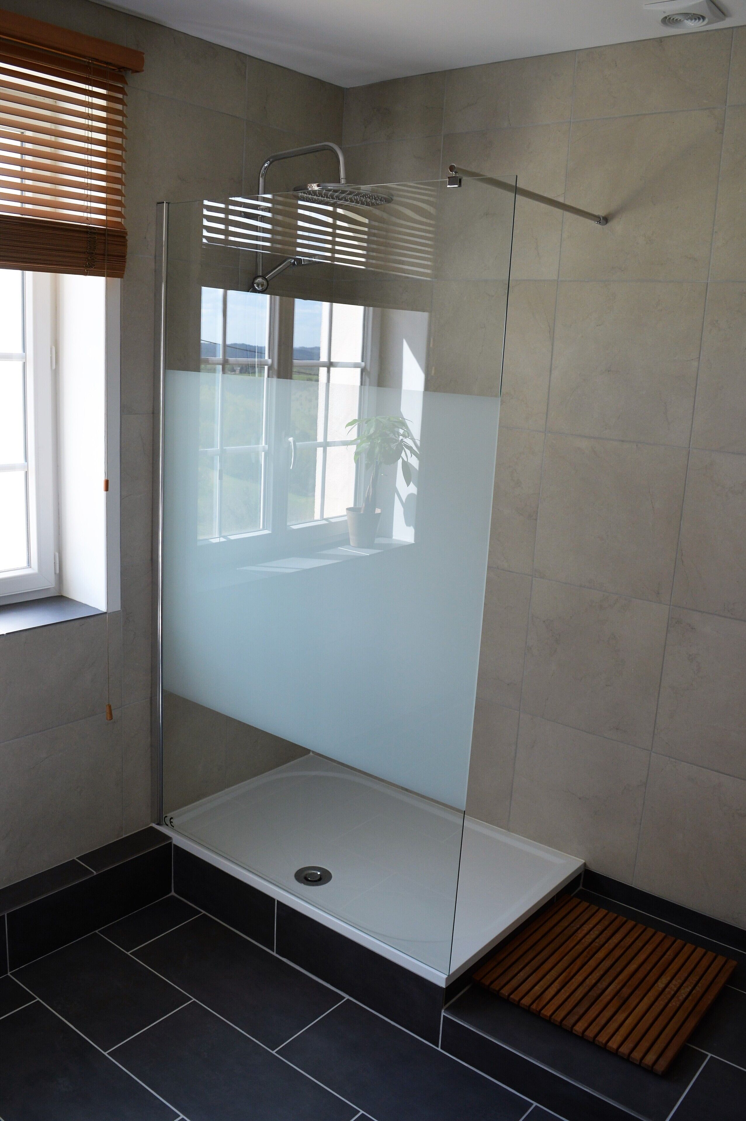 Une salle de bain moderne avec une douche à parois de verre, une fenêtre avec des stores et une plante en pot.