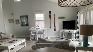 A living room with a round table, white sofas, a dining table with chairs, a TV, and decorative items.