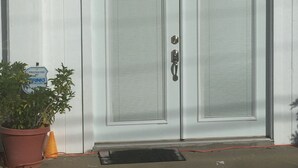 A double door with a metal handle, a potted plant, and a sign on the wall. - Kwik Kabana "Where the Beach Counts" (Galveston)