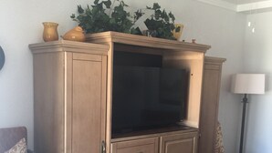 A living room with a wooden entertainment center, a sofa, a chair, and a floor lamp. - Kwik Kabana "Where the Beach Counts" (Galveston)