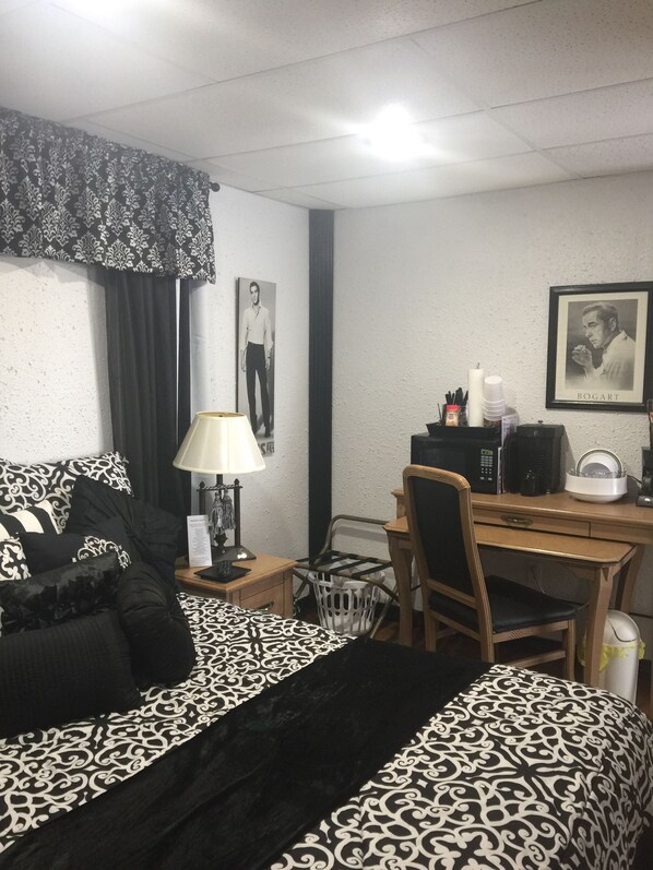 A hotel room with a bed, a desk, a chair, a lamp, and a framed picture on the wall.